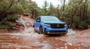 A blue 2023 Honda Pilot TrailSport is shown driving through muddy water.