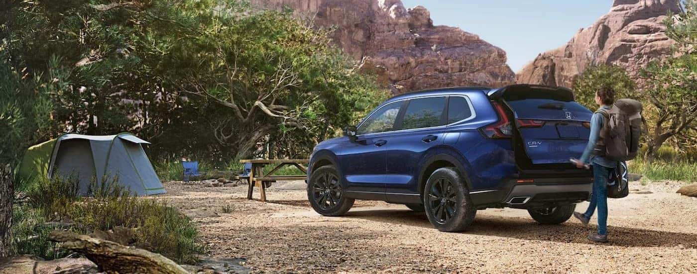 A blue 2025 Honda CR-V Sport Touring Hybrid is shown parked on a campsite.