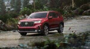 A red 2025 Honda Pilot is shown driving on a rainy day.