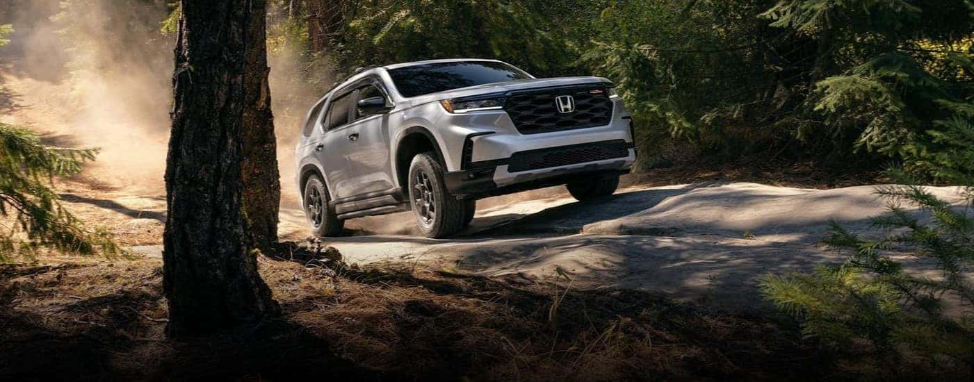 A white 2025 Honda Pilot Trailsport is shown driving off-road.