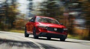 A red 2024 Honda Accord Sport L Hybrid driving to a Honda dealer.