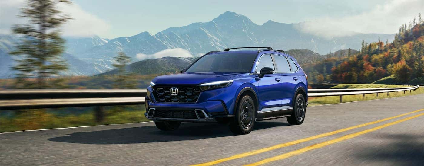 A blue 2024 Honda CR-V Sport Touring Hybrid driving through the mountains.