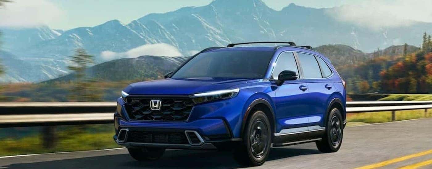 A blue 2024 Honda CR-V Sport Touring is shown driving on a highway.