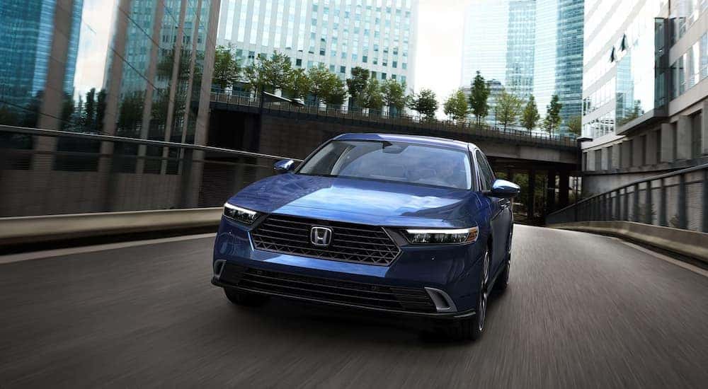A blue 2025 Honda Accord Touring Hybrid driving through a city street.
