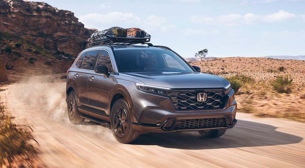 A grey 2025 Honda CR-V Hybrid for sale driving down a desert road.