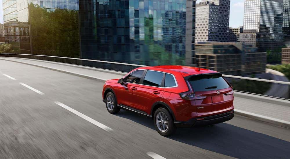 Rear angle view of a red 2025 Honda CR-V Hybrid driving through a city.