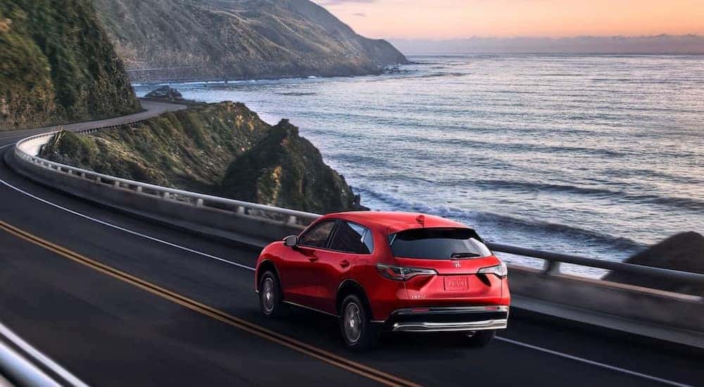 A red 2025 Honda HR-V EX-L is shown driving near an ocean.