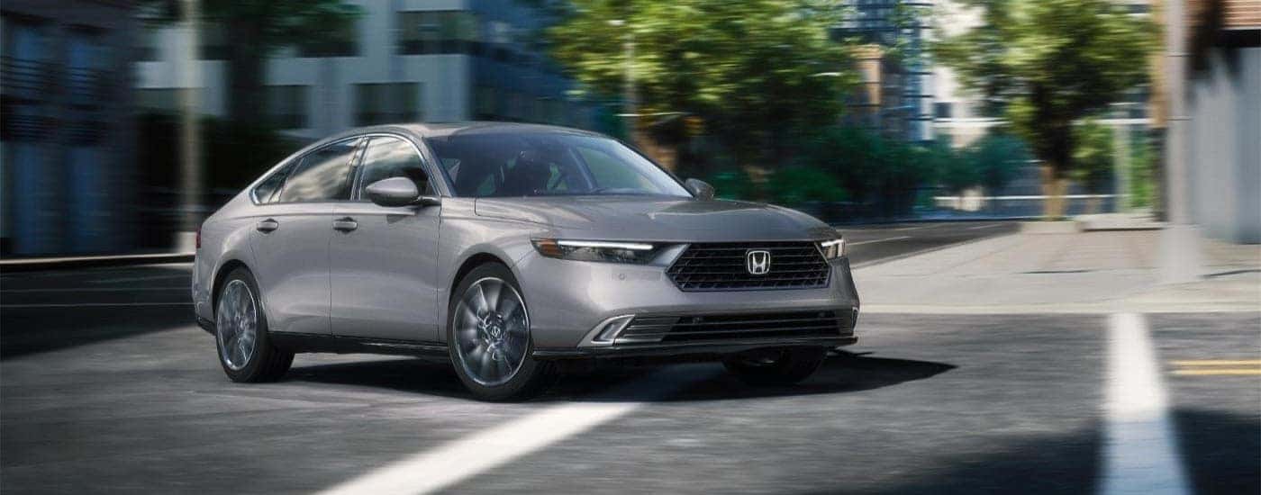 A grey 2025 Honda Accord Touring Hybrid driving through a city after visiting a dealer with a Honda Accord Hybrid for sale in North Richland Hills.