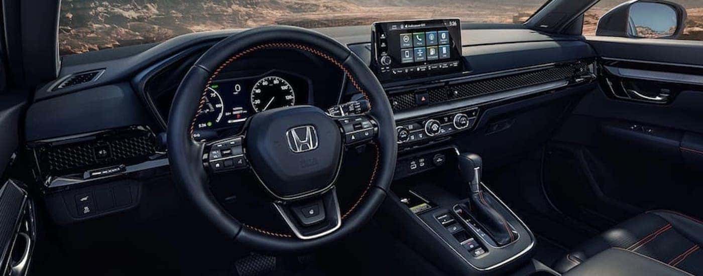The black interior of a 2025 Honda CR-V is shown from the driver's side.