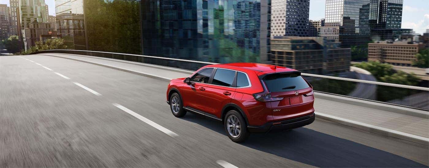Rear view of a red 2025 Honda CR-V driving in a city.