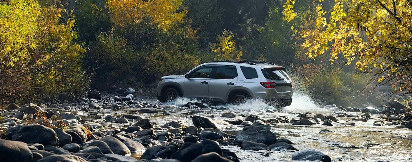 Rear view of a grey 2024 Honda Pilot TrailSport driving over a shallow river.
