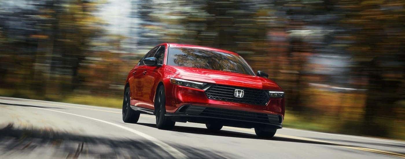 A red 2025 Honda Accord Hybrid for sale near Southlake is shown driving on a highway.