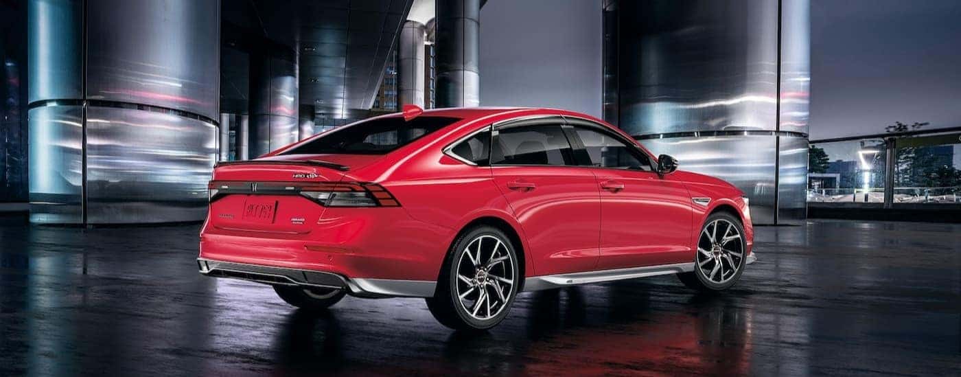 A red 2025 Honda Accord Touring Hybrid is shown parked near metal pillars.