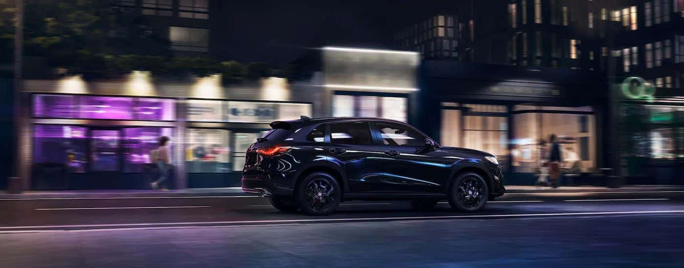 A black 2025 Honda HR-V Sport is driving on a city street at night.