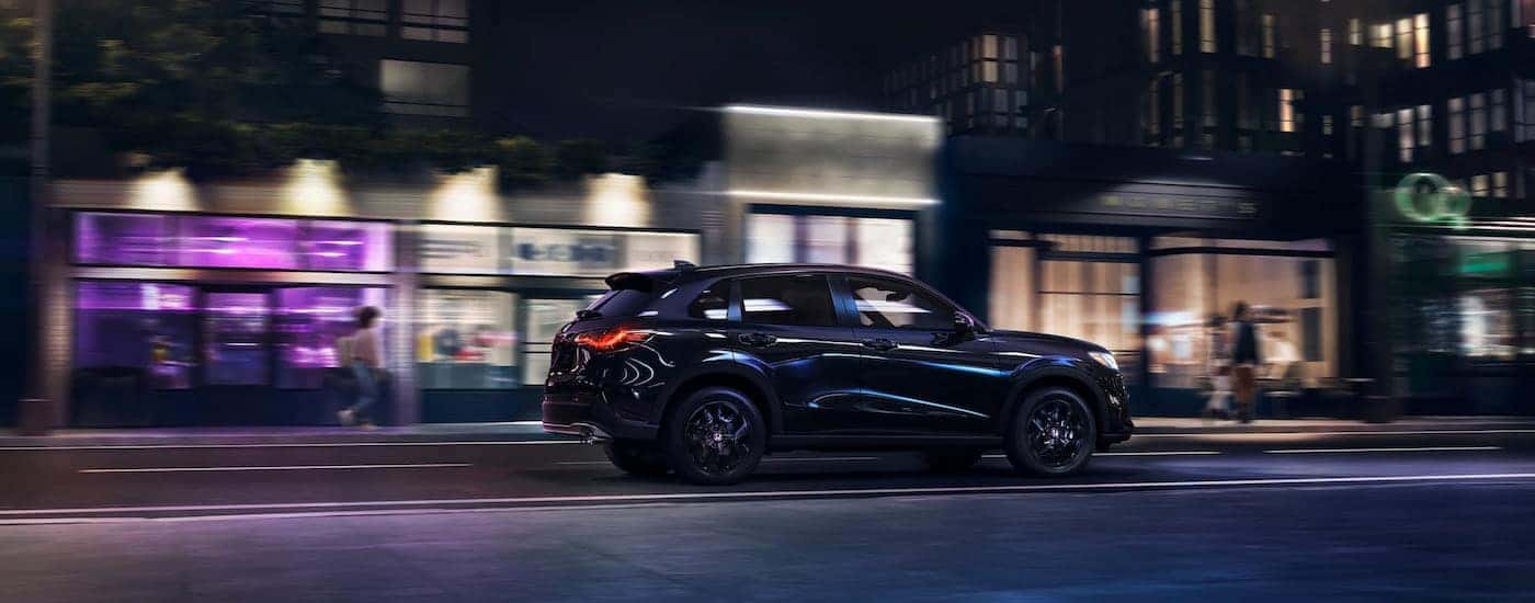 Rear side angle view of a black 2025 Honda HR-V Sport driving through a city.