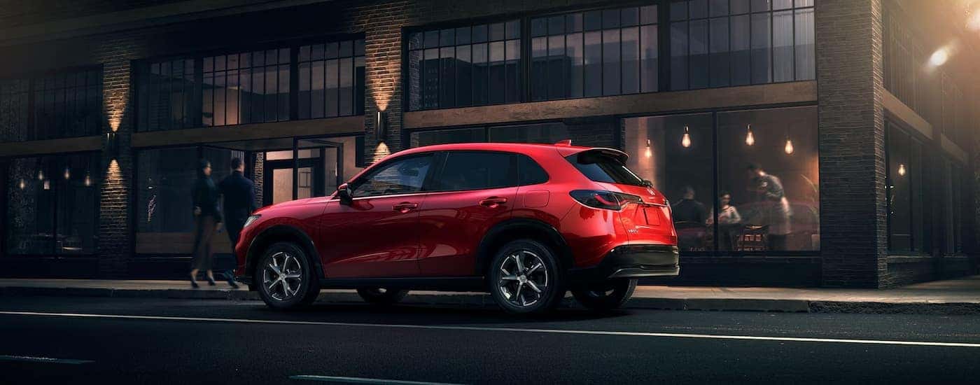 Side angle view of a red 2025 Honda HR-V parked by a city curb.