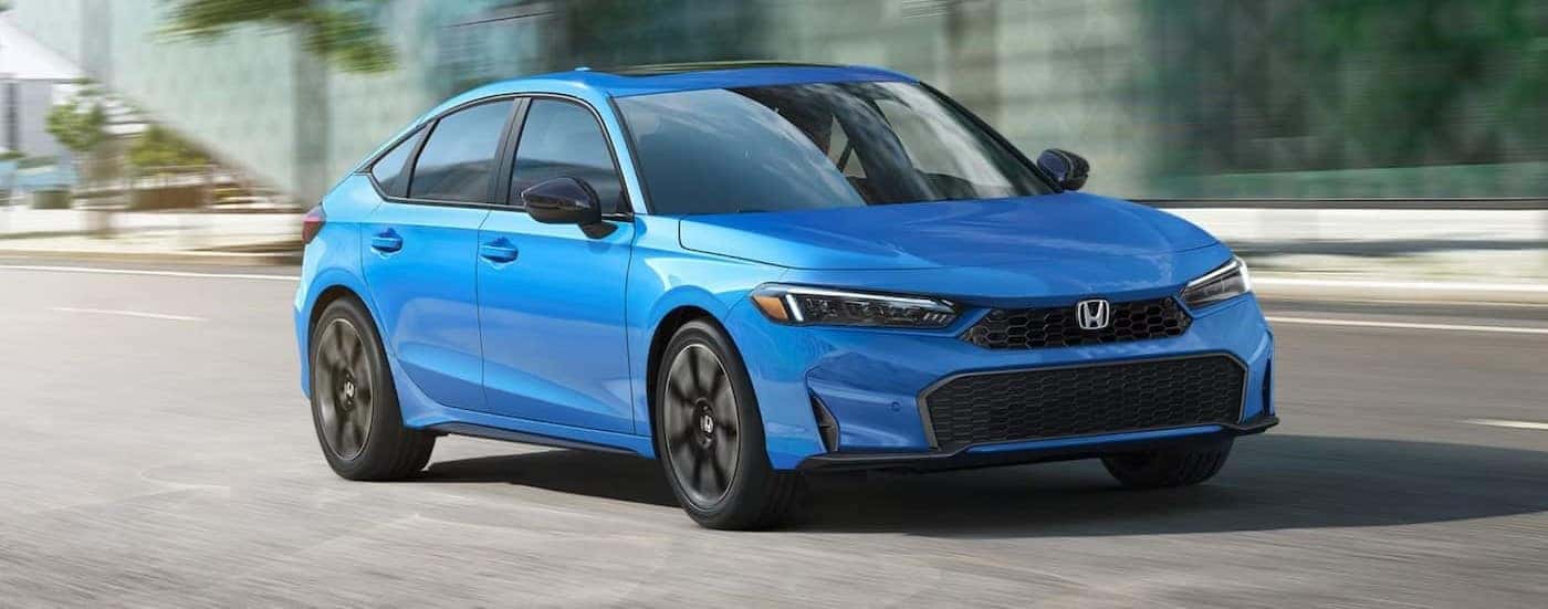 A blue 2025 Honda Civic Hatchback driving in a city.