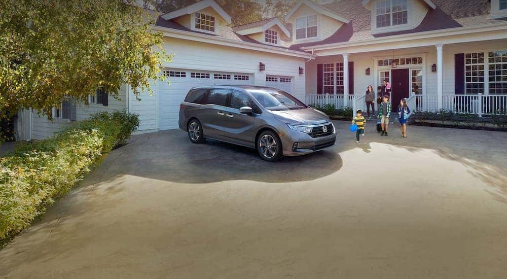 A silver 2025 Honda Odyssey for sale parked near a family.
