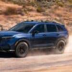 A blue 2026 Honda CR-V TrailSport Hybrid driving off-road.