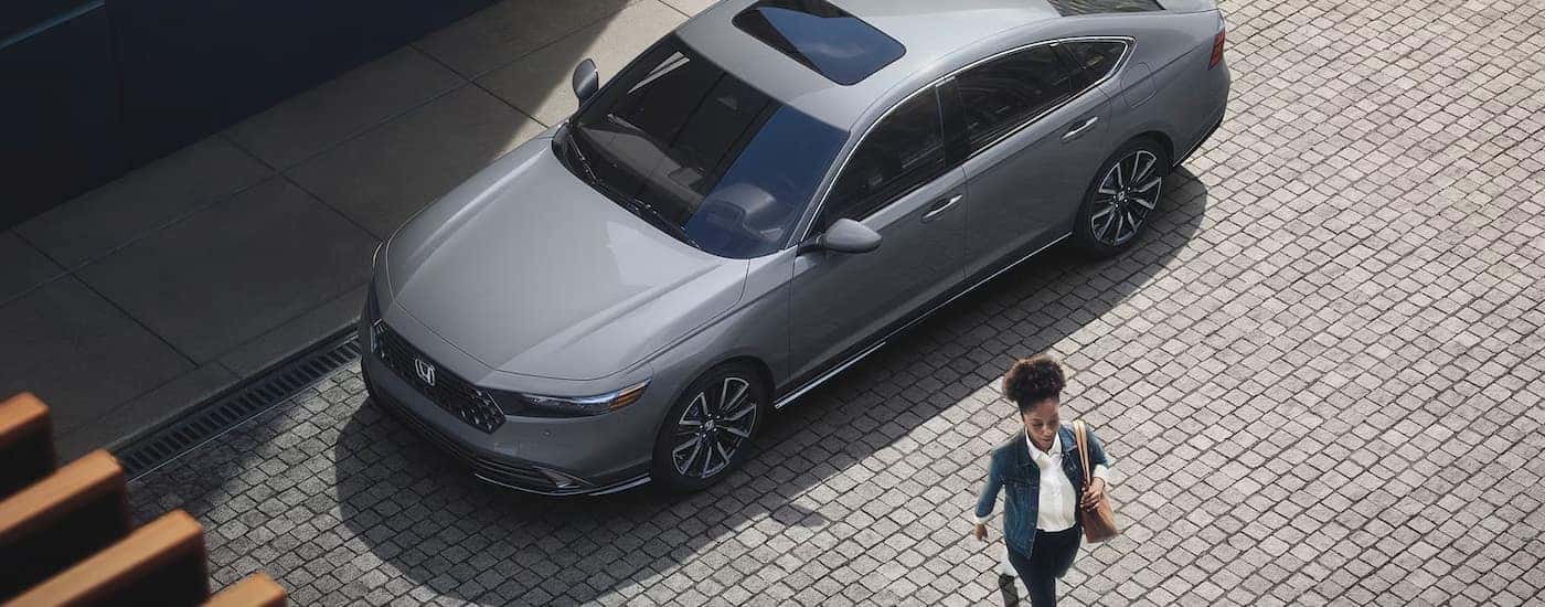 Overhead view of a woman walking past a silver 2025 Honda Accord Hybrid for sale near Grapevine.