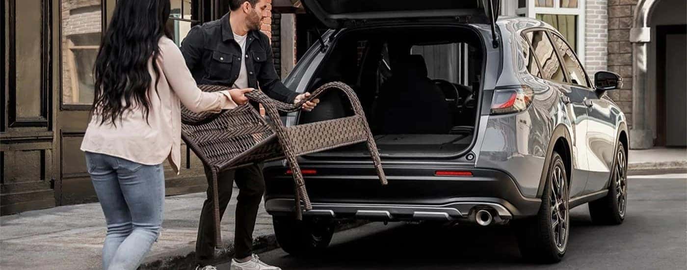Two people putting a chair in the rear cargo area of a silver 2025 Honda HR-V Sport.