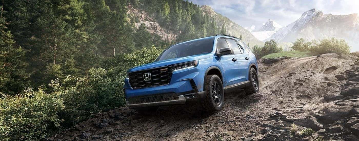 A blue 2023 Honda Pilot TrailSport idriving on a rocky path.