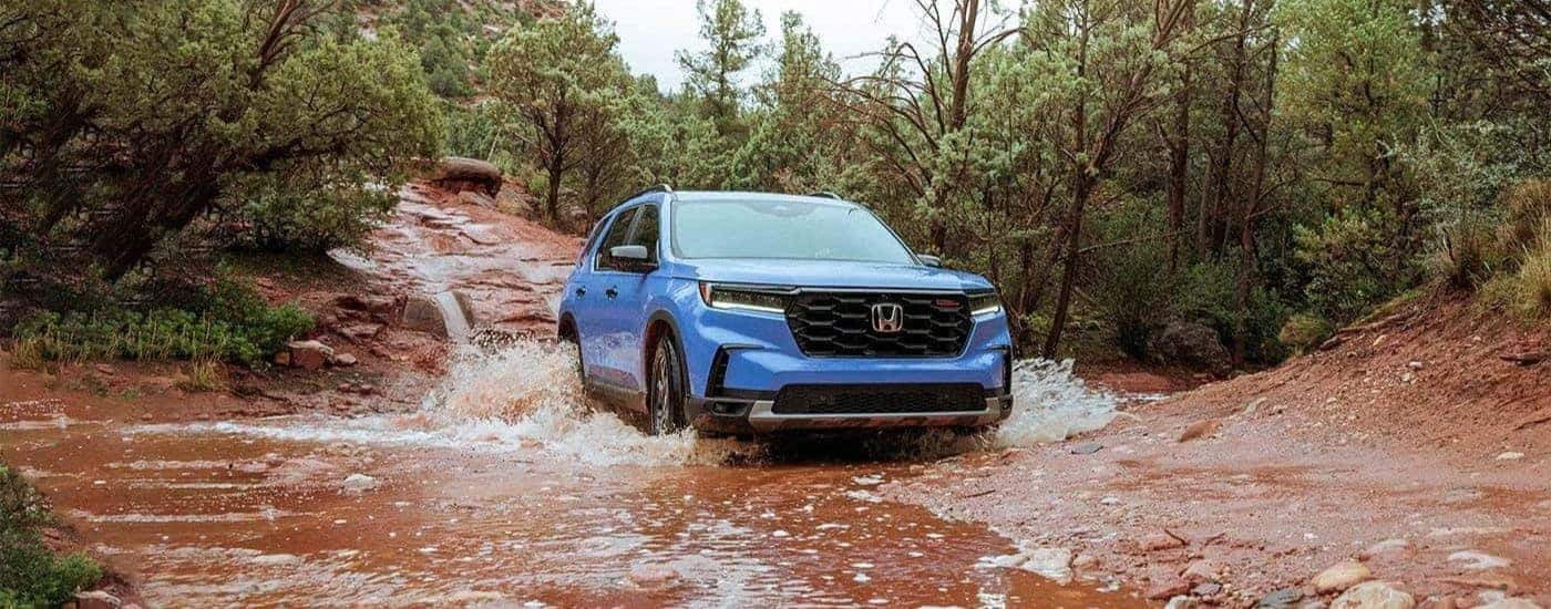 A blue 2023 Honda Pilot TrailSport is shown driving through muddy water.