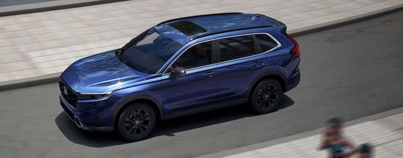 A blue 2025 Honda CR-V Sport Touring Hybrid is shown driving on a city street.