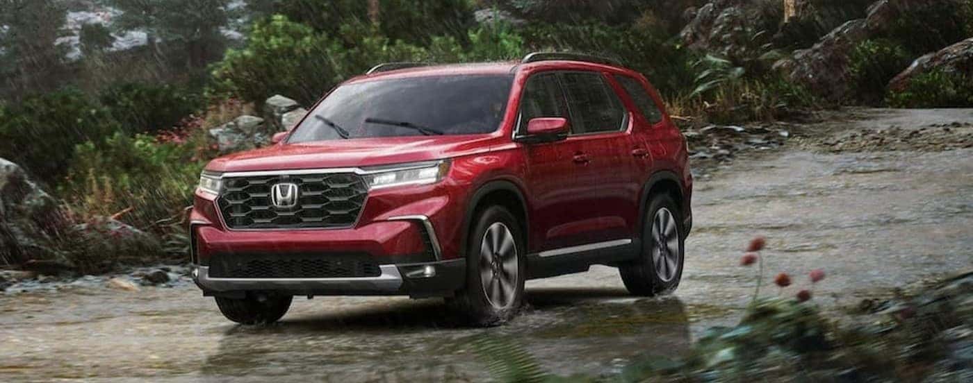 A red 2025 Honda Pilot for sale driving on a rainy day.