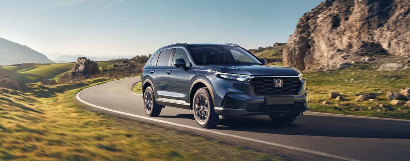A blue 2025 Honda CR-V Hybrid for sale is rounding a corner.