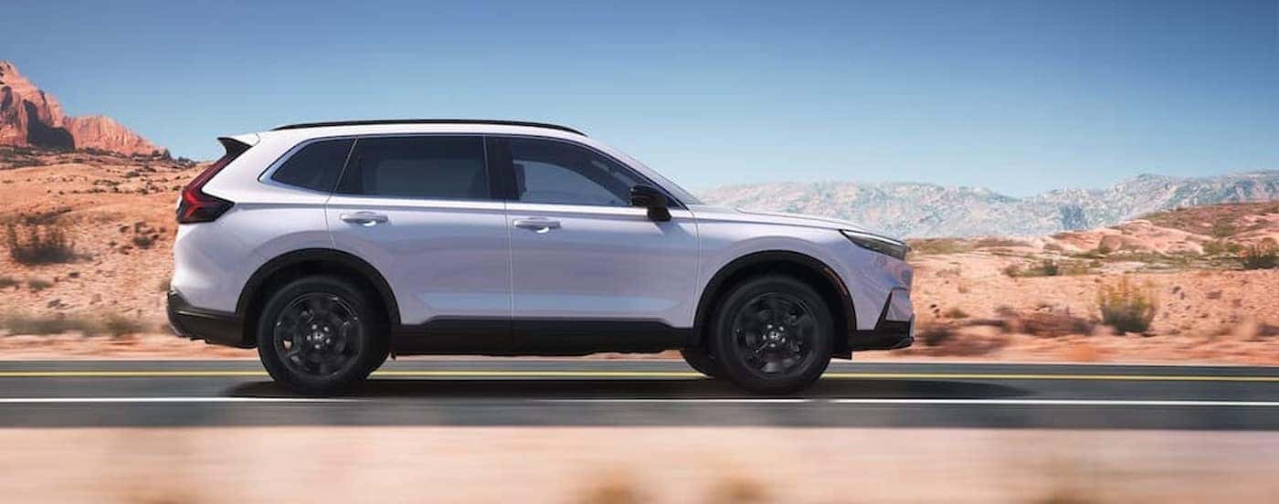 A white 2025 Honda CR-V Hyrbid for sale near Fort Worth driving on a highway.