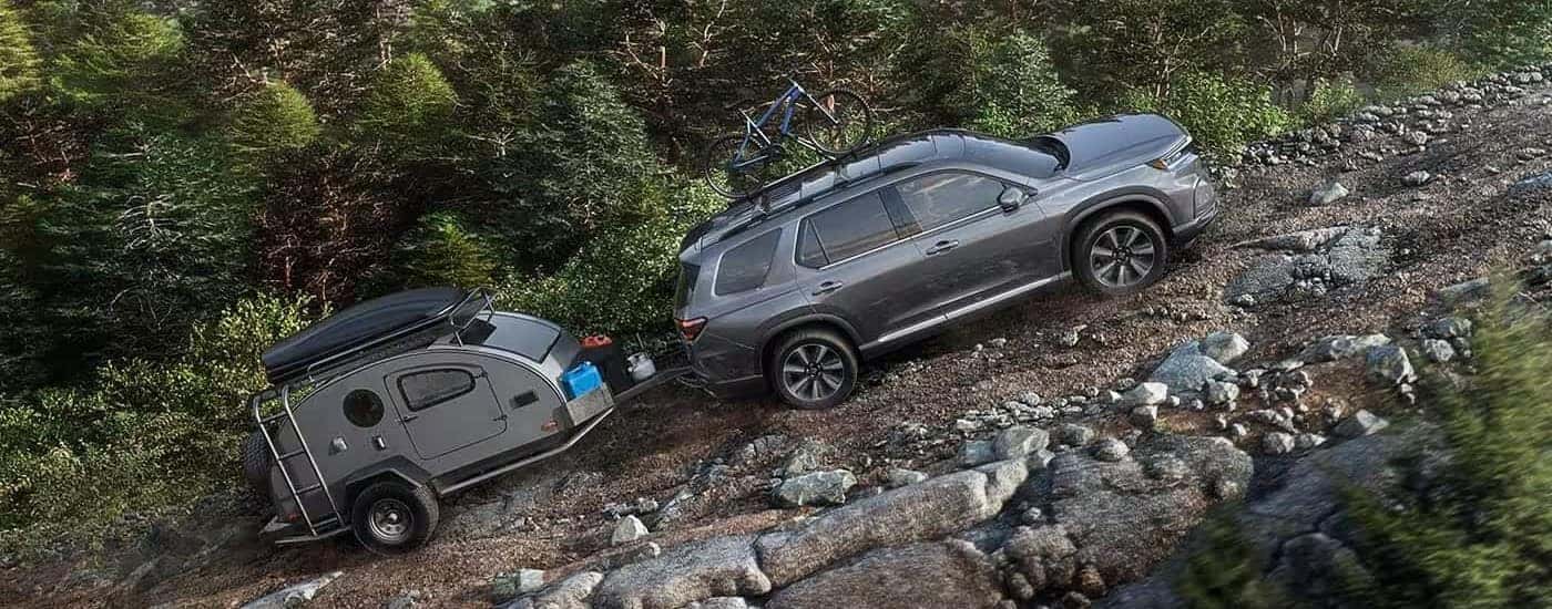 A gray 2023 Honda Pilot is shown driving uphill on off-road terrain.
