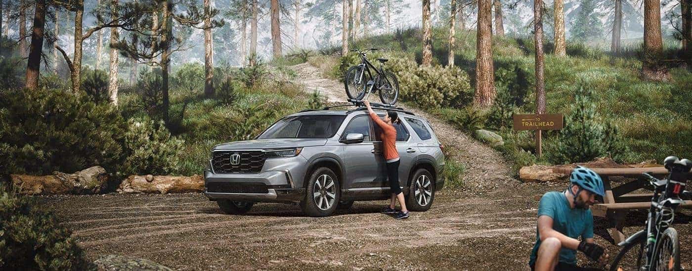 A person placing a bicycle on top of a grey 2023 Honda Pilot for sale near Colleyville.