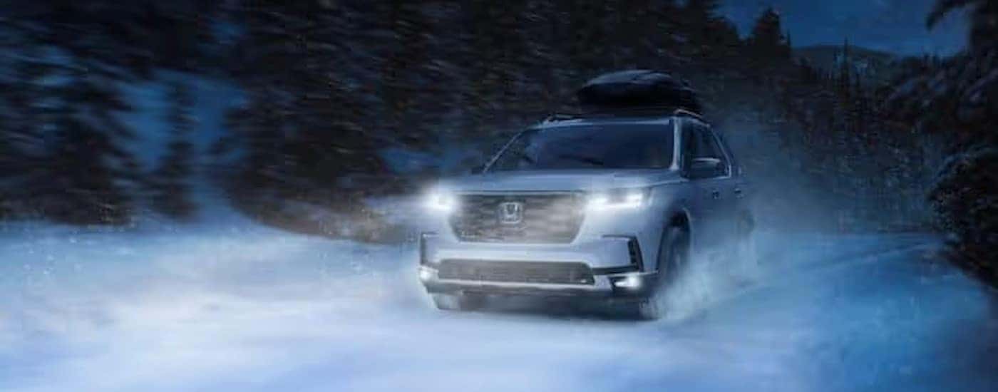 A white 2024 Honda Pilot for sale near Southlake driving down a snowy road.