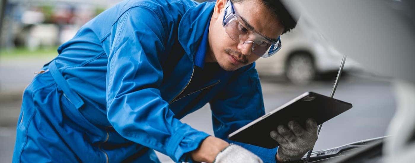 A mechanic in blue coveralls inspecting a car's engine at a Honda service center.