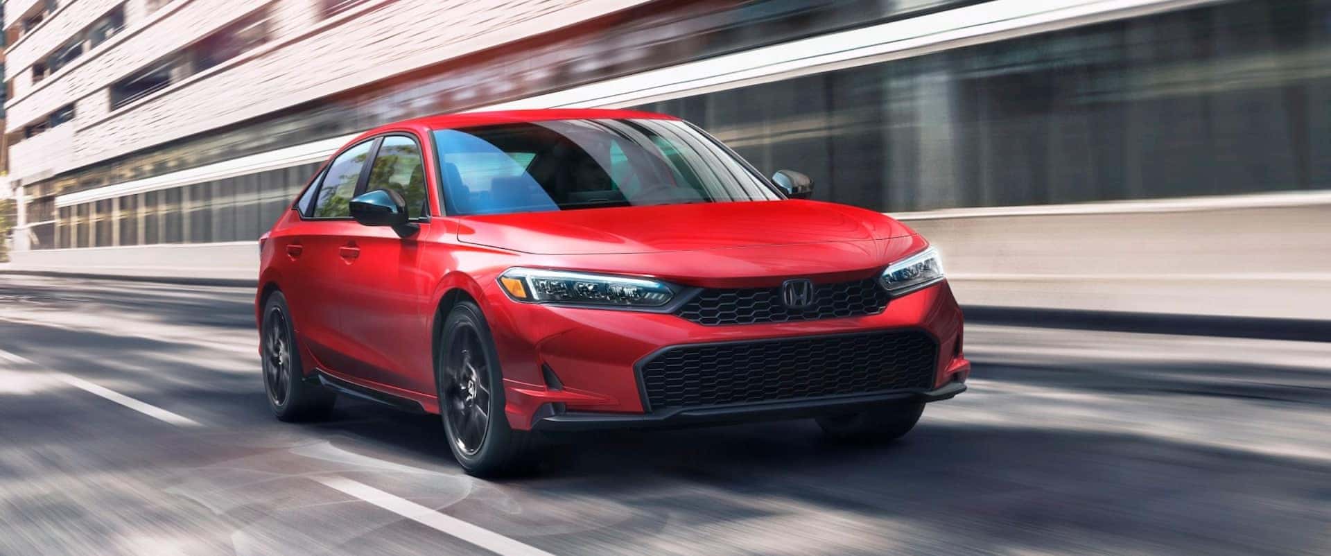 Red 2026 Honda Civic Sport driving down a road.