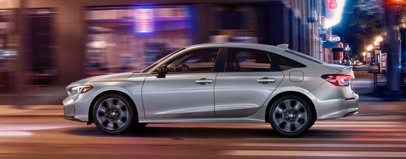 A silver 2025 Honda Civic driving down a city street at night