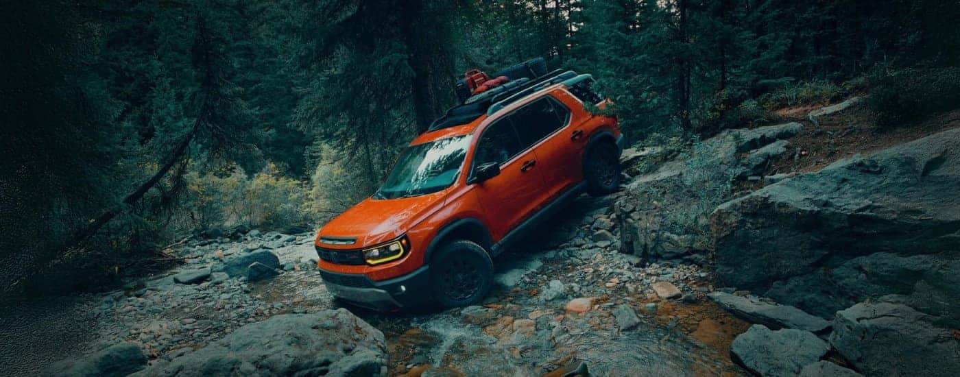 An orange 2026 Honda Passport Elite TrailSport off-roading on rocks