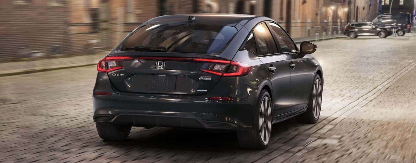 Rear of a black 2026 Honda Civic Sport Touring Hybrid driving down a city street.
