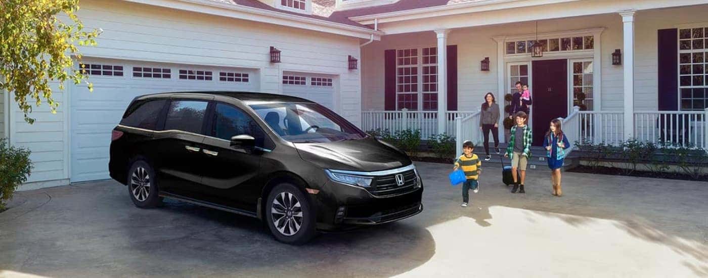 A black 2025 Honda Odyssey parked in a driveway with a family getting inside