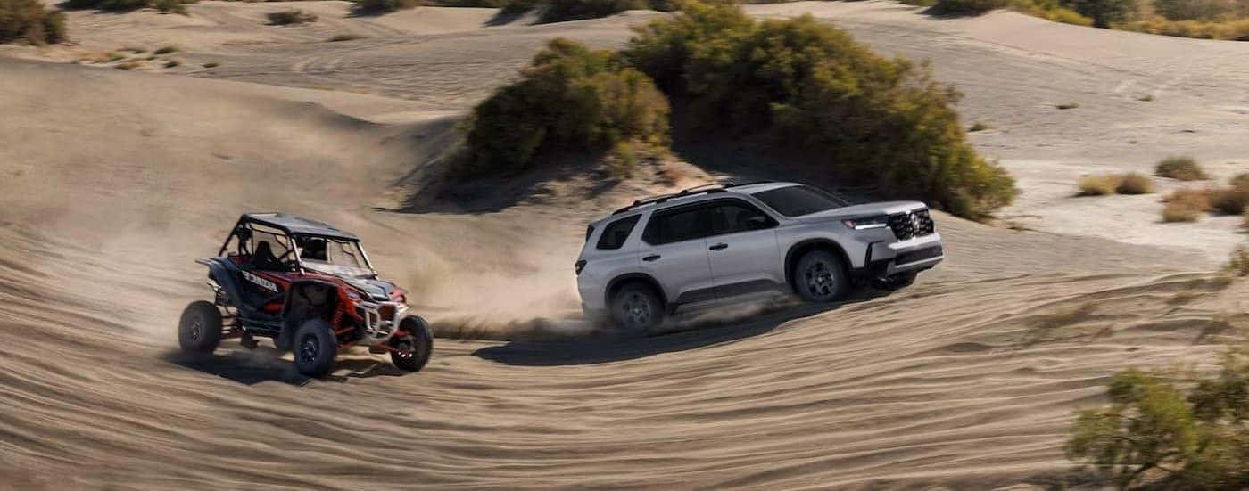 A silver 2025 Honda Pilot TrailSport off-roading near a UTV.