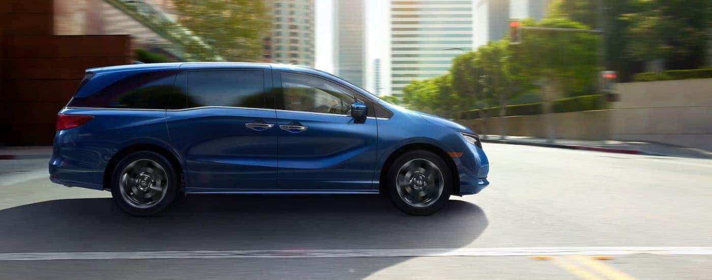 Side of a dark blue 2026 Honda Odyssey driving down a road.