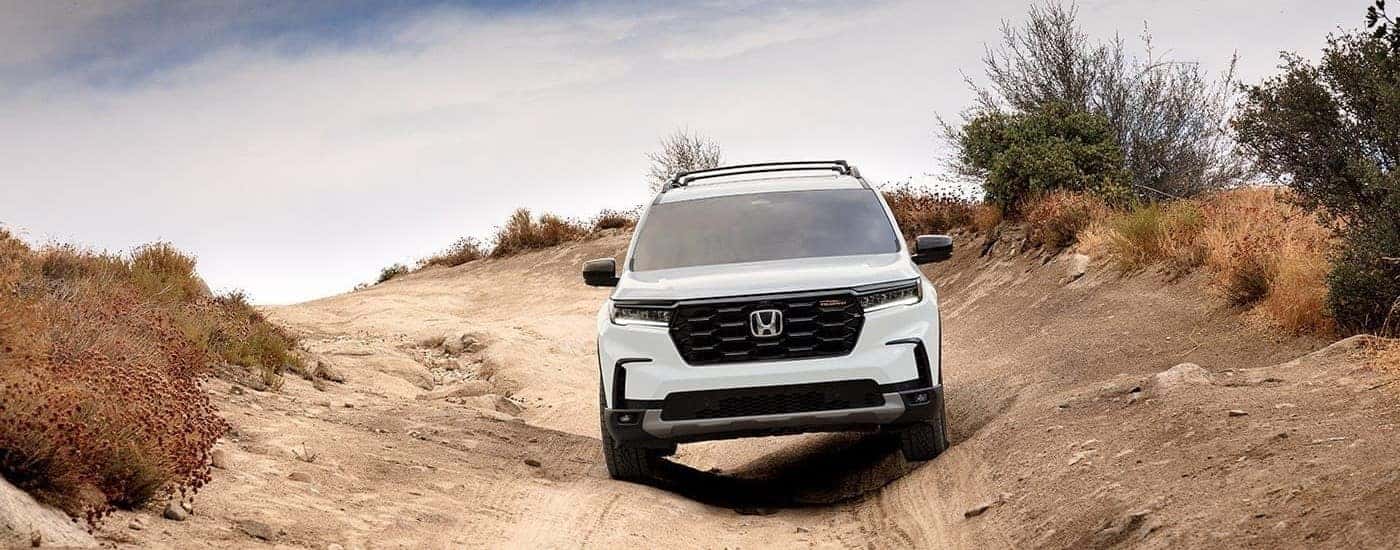 Front of a white 2026 Honda Pilot TrailSport driving off-road.