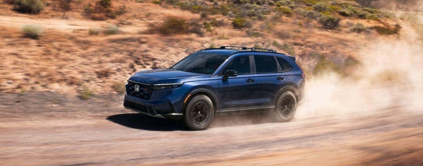 Dark blue 2026 Honda CR-V TrailSport Hybrid driving off-road.