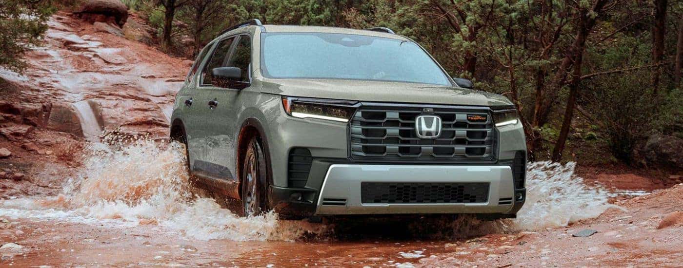 Green 2026 Honda Pilot driving through a muddy river.