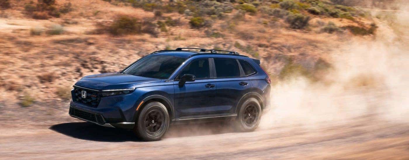 Blue 2026 Honda CR-V Hybrid TrailSPort sending up dust on a dirt road.