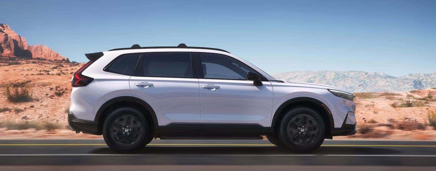 A white 2026 CR-V Hybrid driving on a paved desert road.