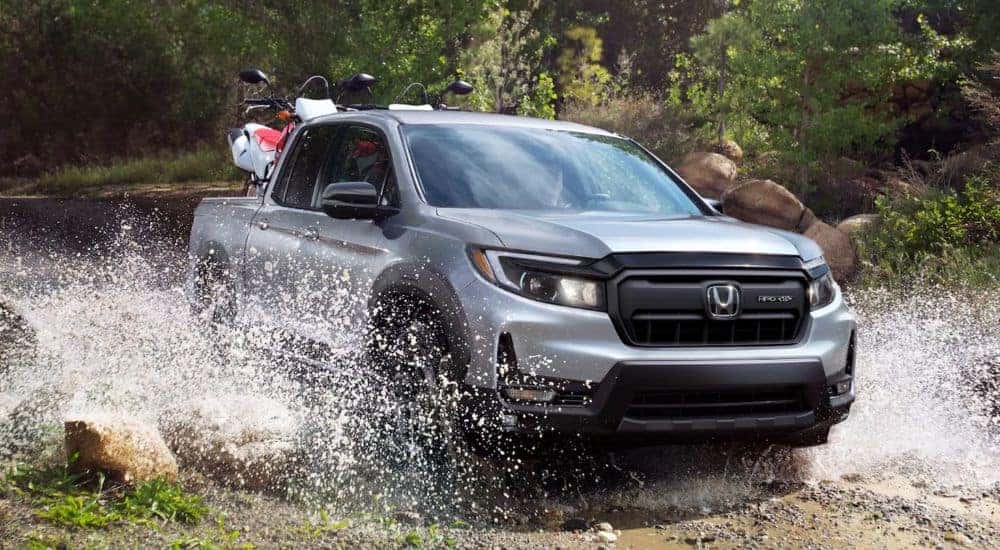 A silver 2026 Honda Ridgeline shown driving through a puddle.