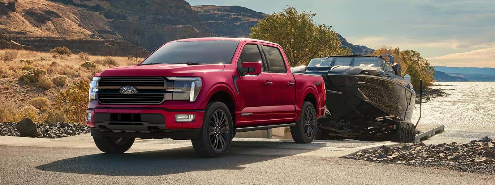 2026 Ford F-150 pickup truck towing a large boat on a trailer near a lakeside road, highlighting full size truck capability and exterior design.
