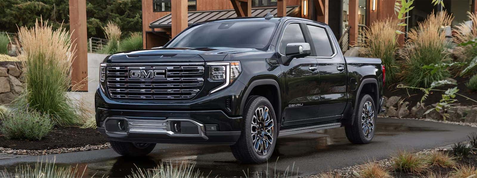 2026 GMC Sierra 1500 Denali parked in a modern outdoor setting, highlighting premium exterior design and bold chrome grille.